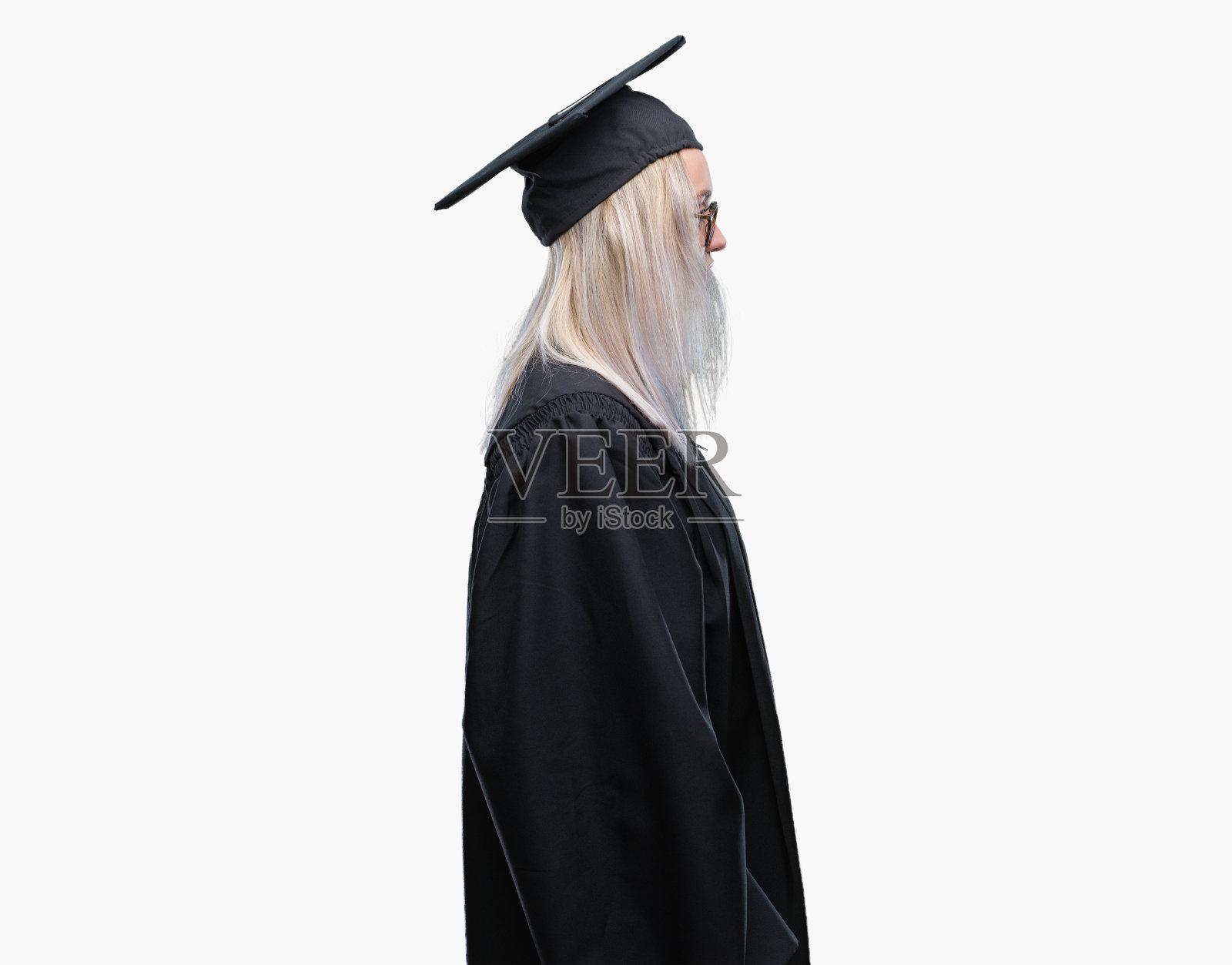 年轻的金发女人穿着毕业制服孤立的背景看向一边，放松的侧面姿势与自然的脸自信的微笑。照片摄影图片