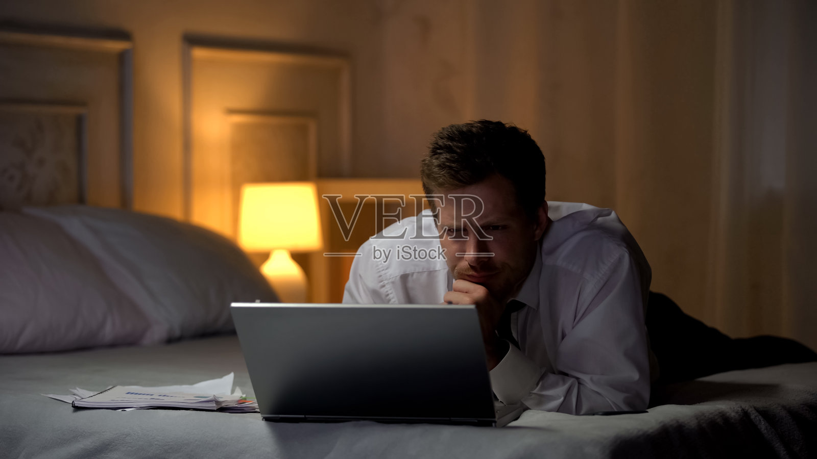 精疲力竭的工程师躺在床上，晚上用笔记本电脑工作，看邮件照片摄影图片