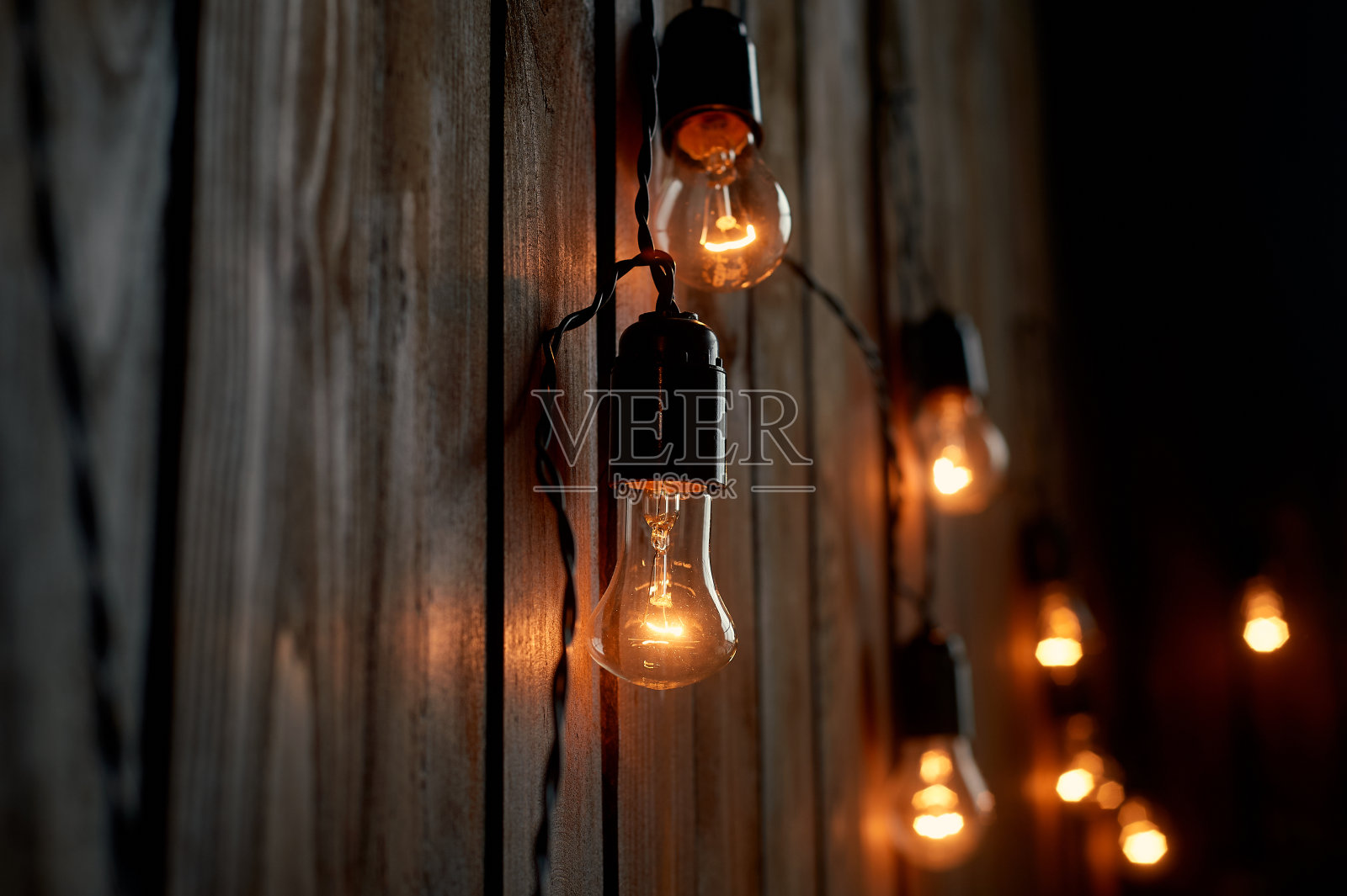 爱迪生的灯泡挂在一根长电线上。温暖的黄色灯光。复古的照片摄影图片