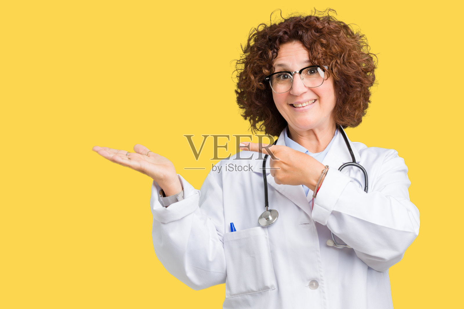 中年资深女医生在孤立的背景下惊讶和微笑的相机，同时提出与手指。照片摄影图片