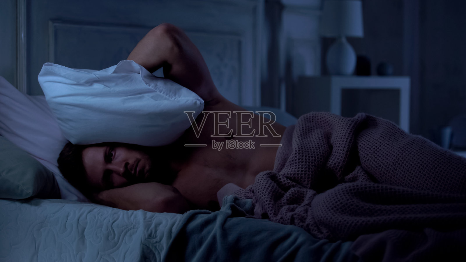 年轻男性失眠，吵闹的邻居听音乐，烦恼照片摄影图片