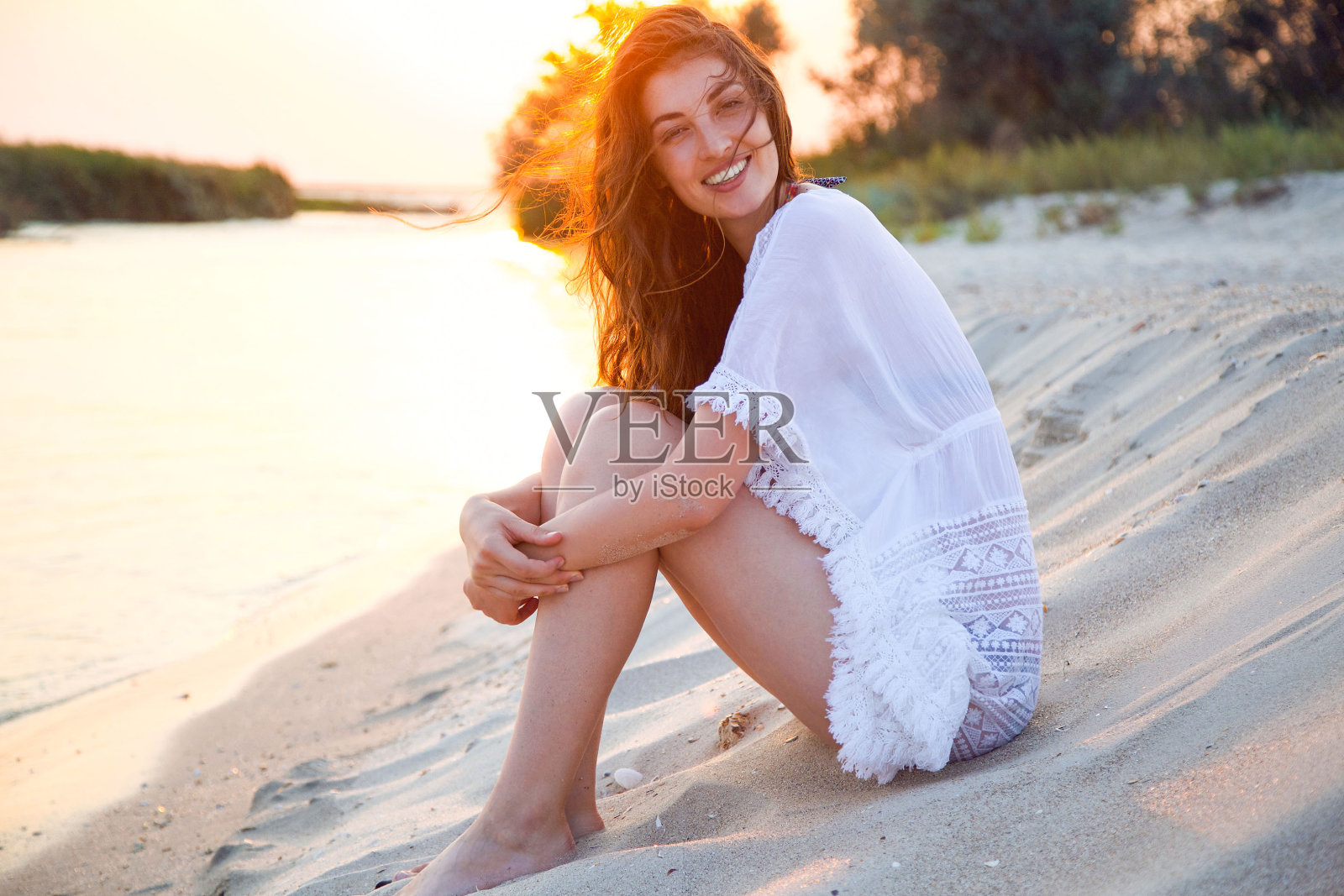 年轻的女人穿着白色的夏装在沙滩上。照片摄影图片