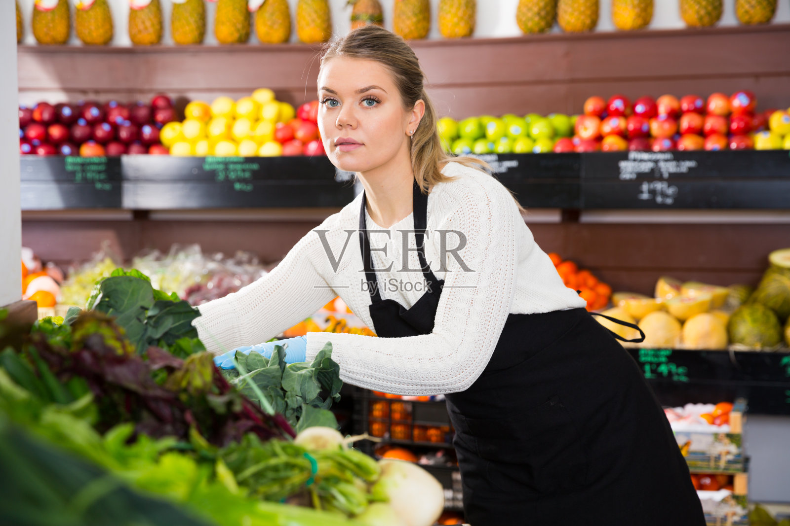 年轻的女售货员戴着手套，正在加工新鲜的绿叶蔬菜和莴苣照片摄影图片