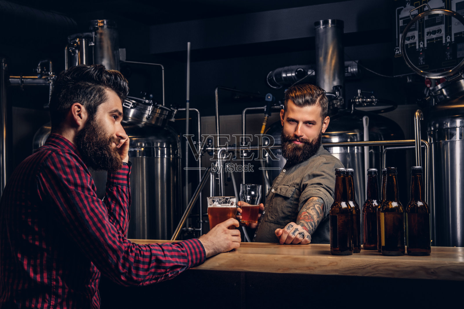 两个留着胡子的时髦嬉皮士朋友在一家独立酿酒厂一起喝精酿啤酒。照片摄影图片