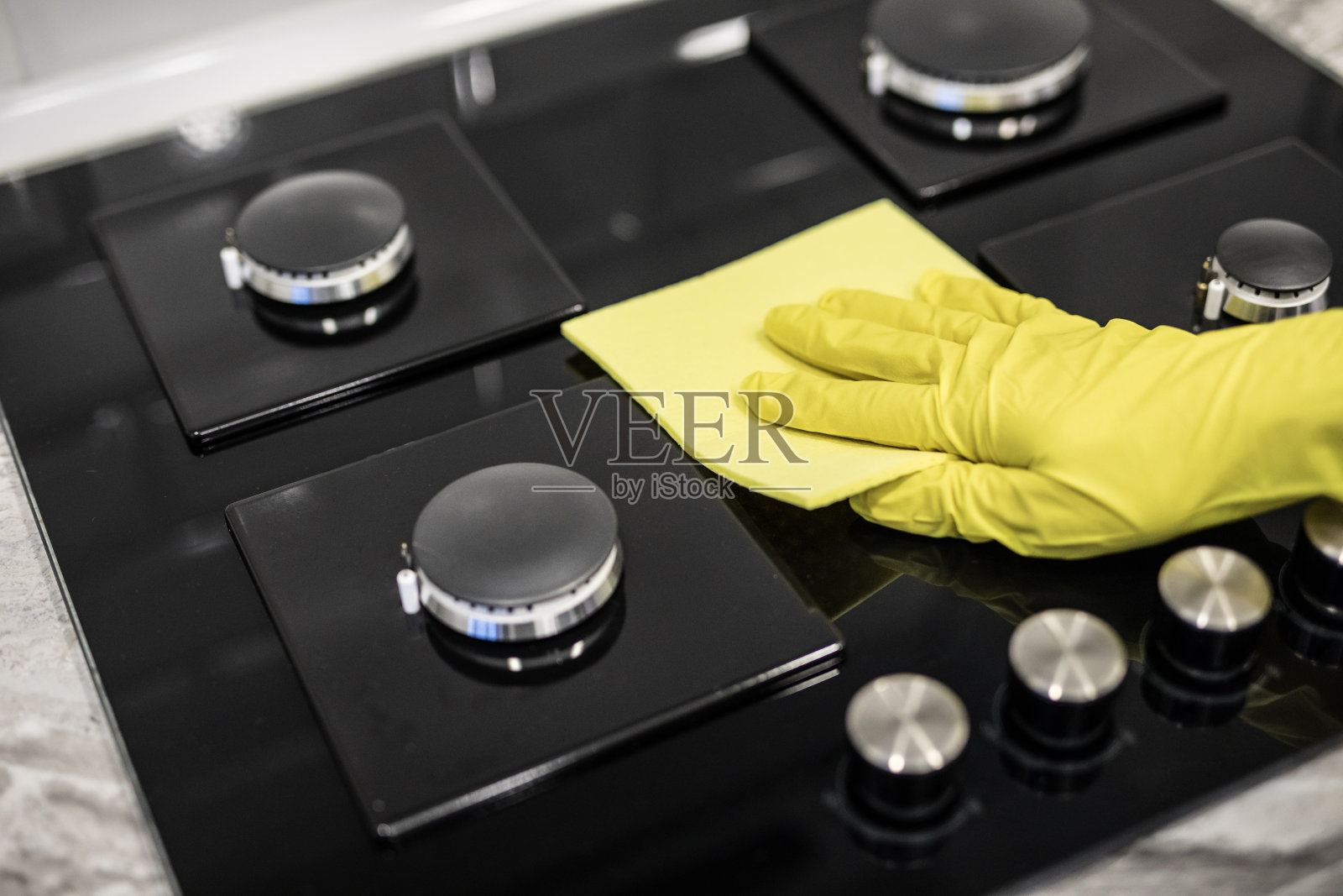 厨房里，一名妇女用黄色的超细纤维布擦拭玻璃陶瓷炉。照片摄影图片