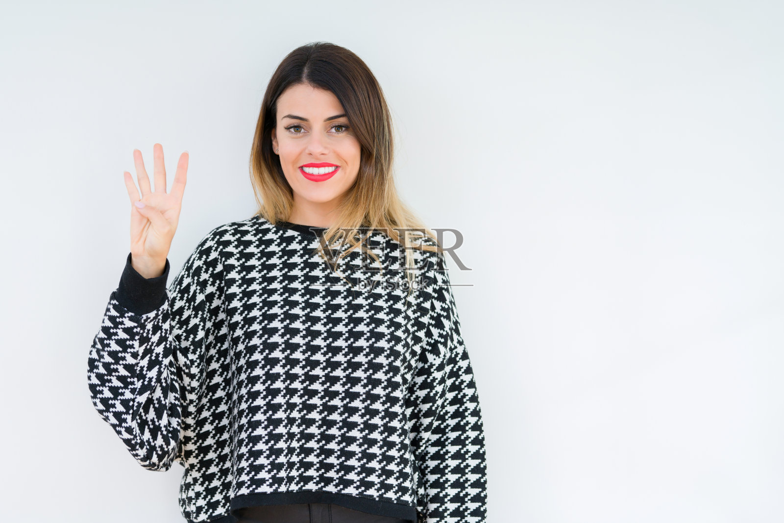 年轻女子穿着休闲毛衣在孤立的背景显示和指着第四个手指，同时自信和快乐的微笑。照片摄影图片