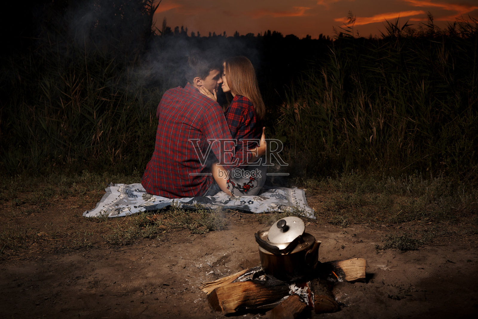 傍晚时分，一对相爱的浪漫情侣在湖边的炉火旁。照片摄影图片