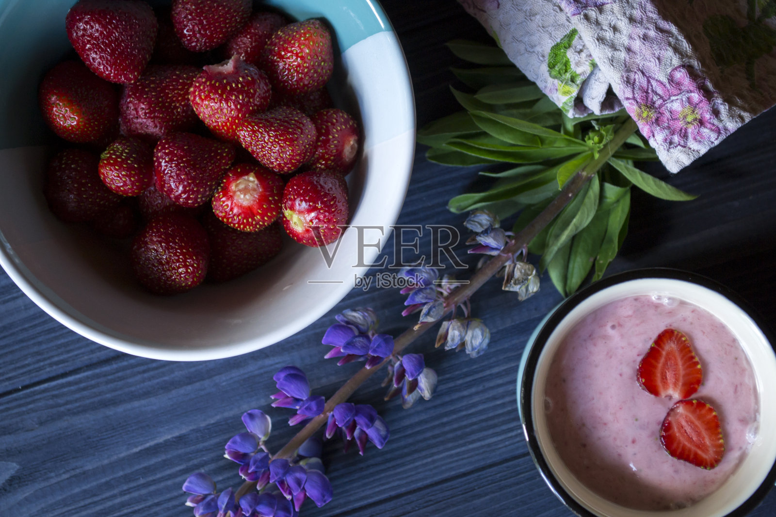 草莓甜点。一杯新鲜的草莓奶油和一碗成熟的草莓放在深蓝色的木桌上。美丽的食物静物。照片摄影图片