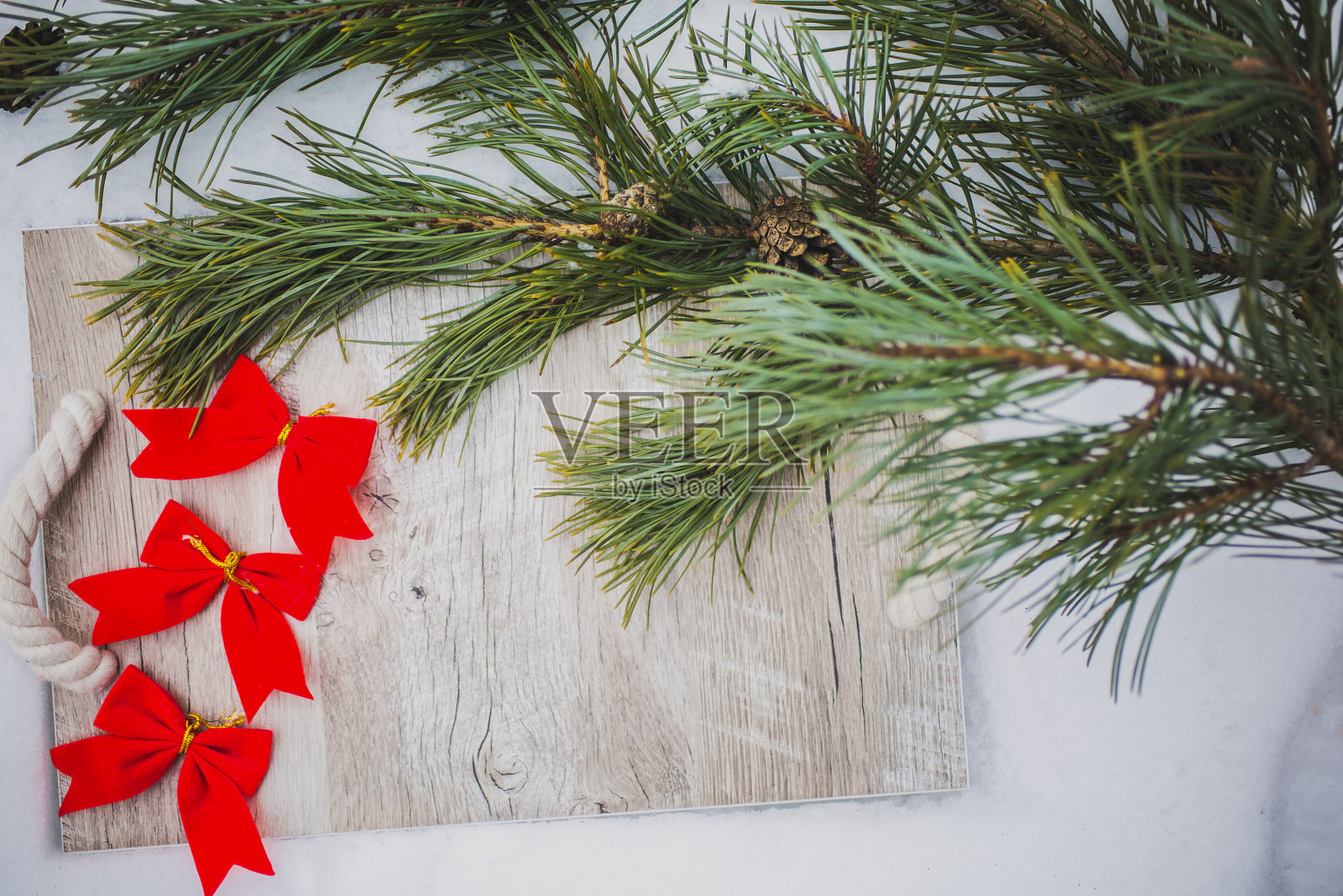 可爱的红色蝴蝶结躺在冬天的户外野餐。松树和木托盘上的雪在森林里。节日快乐。圣诞装饰饰品。浪漫的庆祝活动。本空间的地方。照片摄影图片