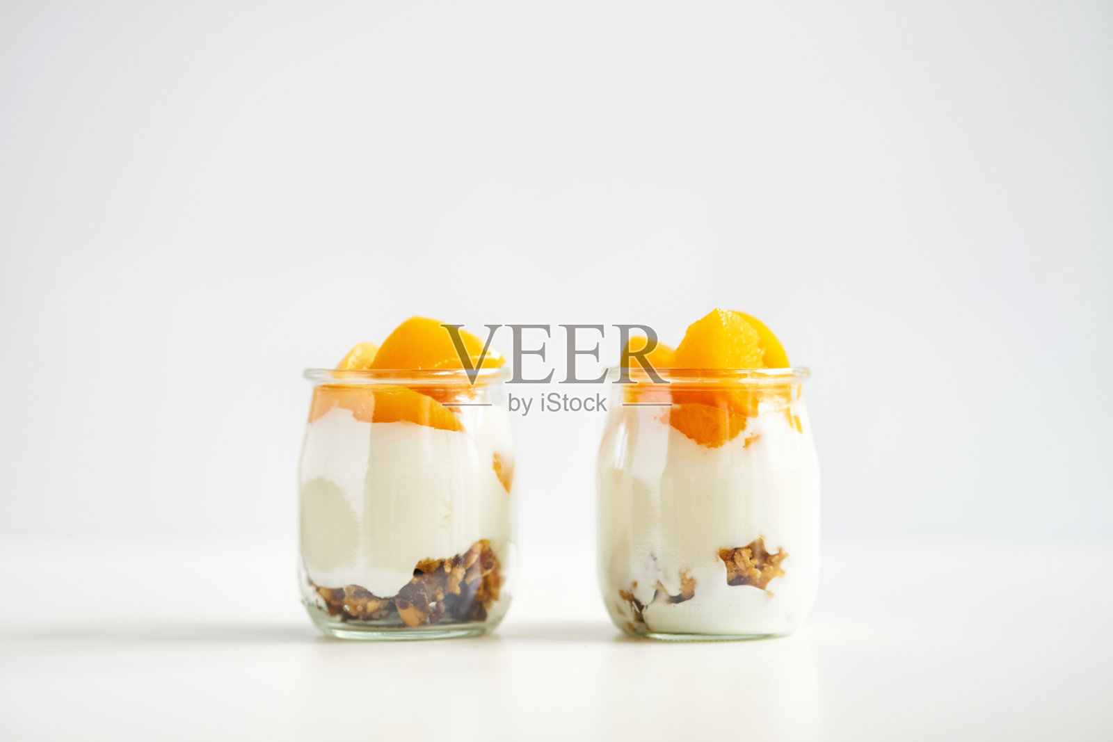 位置对称的希腊酸奶罐与格兰诺拉麦片和杏罐头在白色的背景照片摄影图片