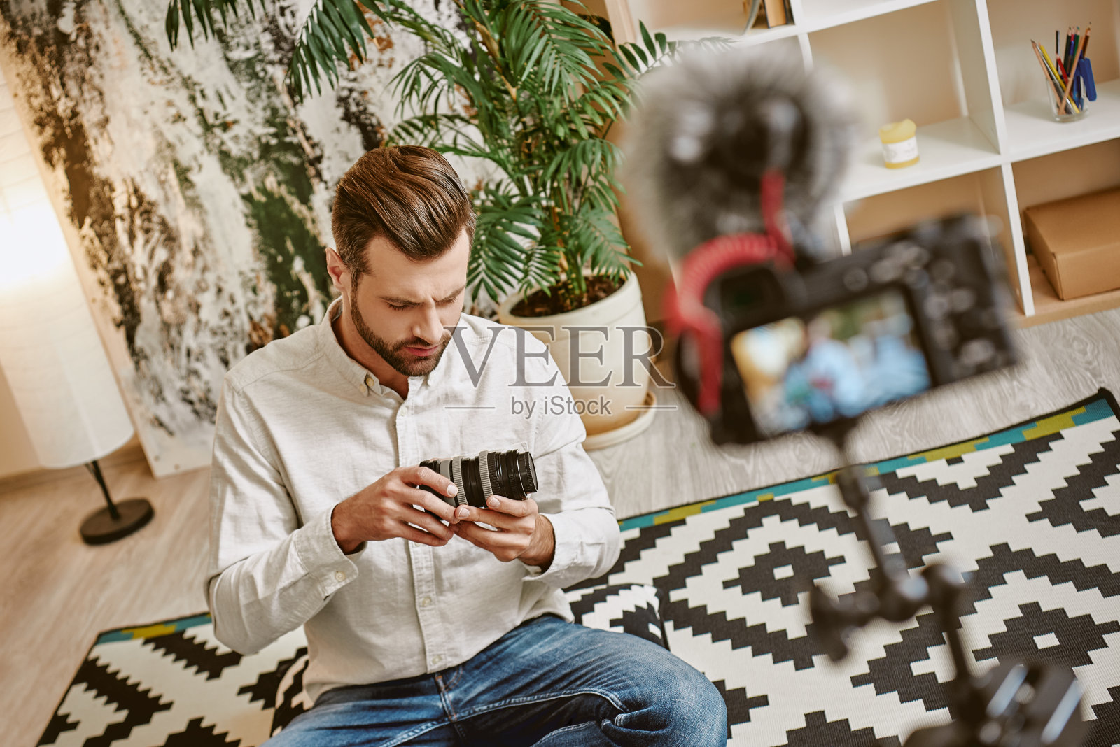 创建内容。年轻的蓄着胡须的博主拿着相机镜头在为他的视频博客录制新视频。照片摄影图片