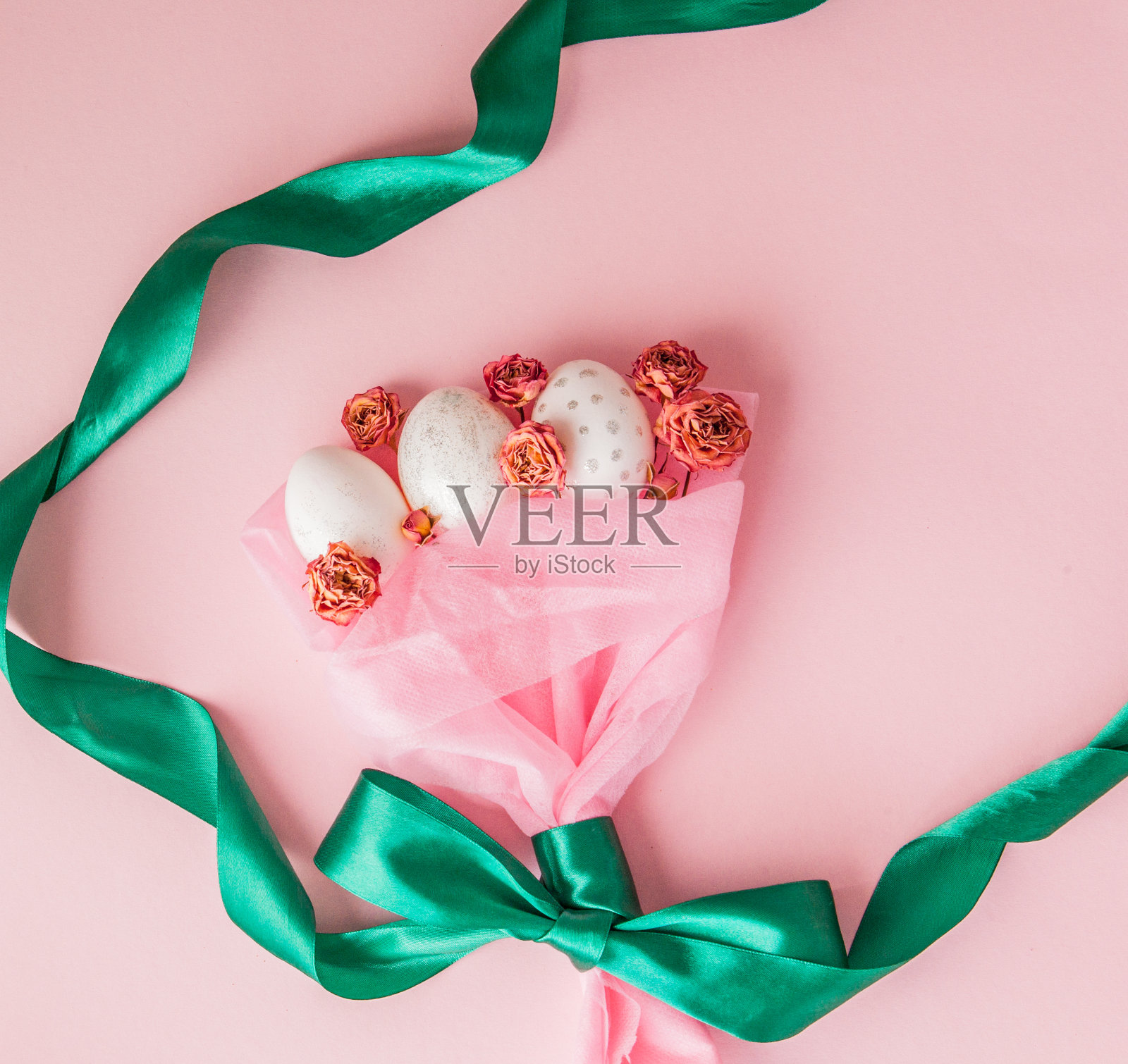 白色的复活节彩蛋放在花束里，粉红色的背景上系着绿色的丝带照片摄影图片
