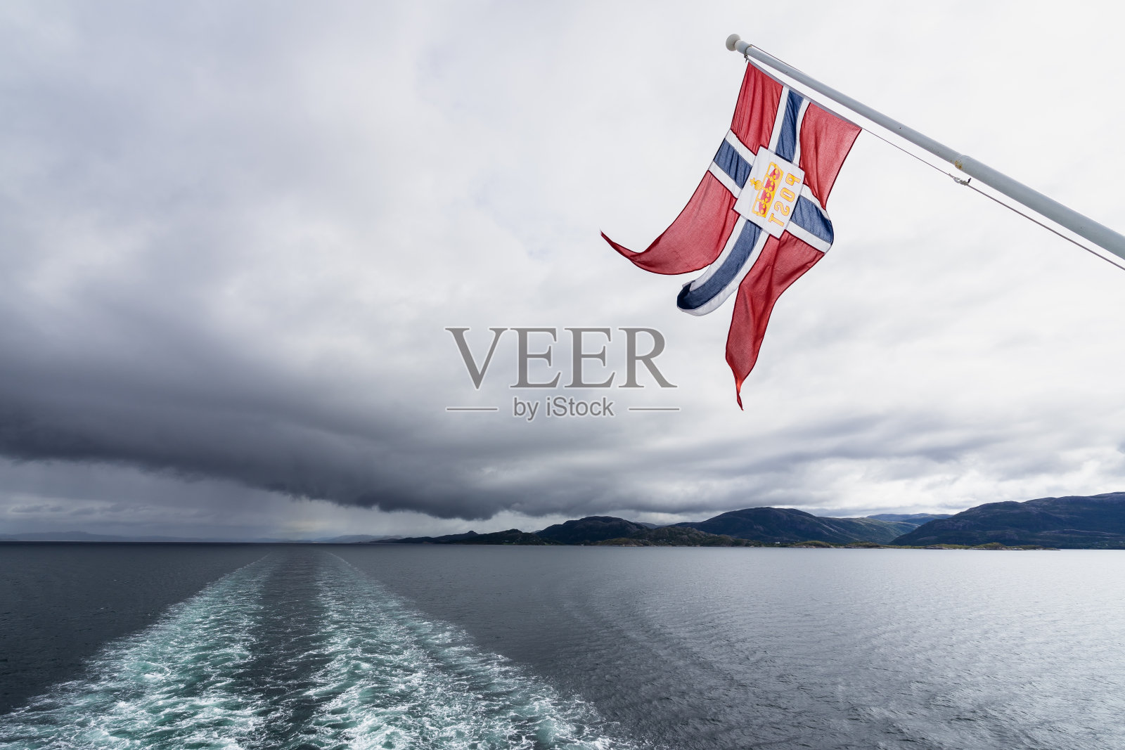 在挪威的峡湾地区，一艘游轮的船尾飘扬着挪威国旗照片摄影图片