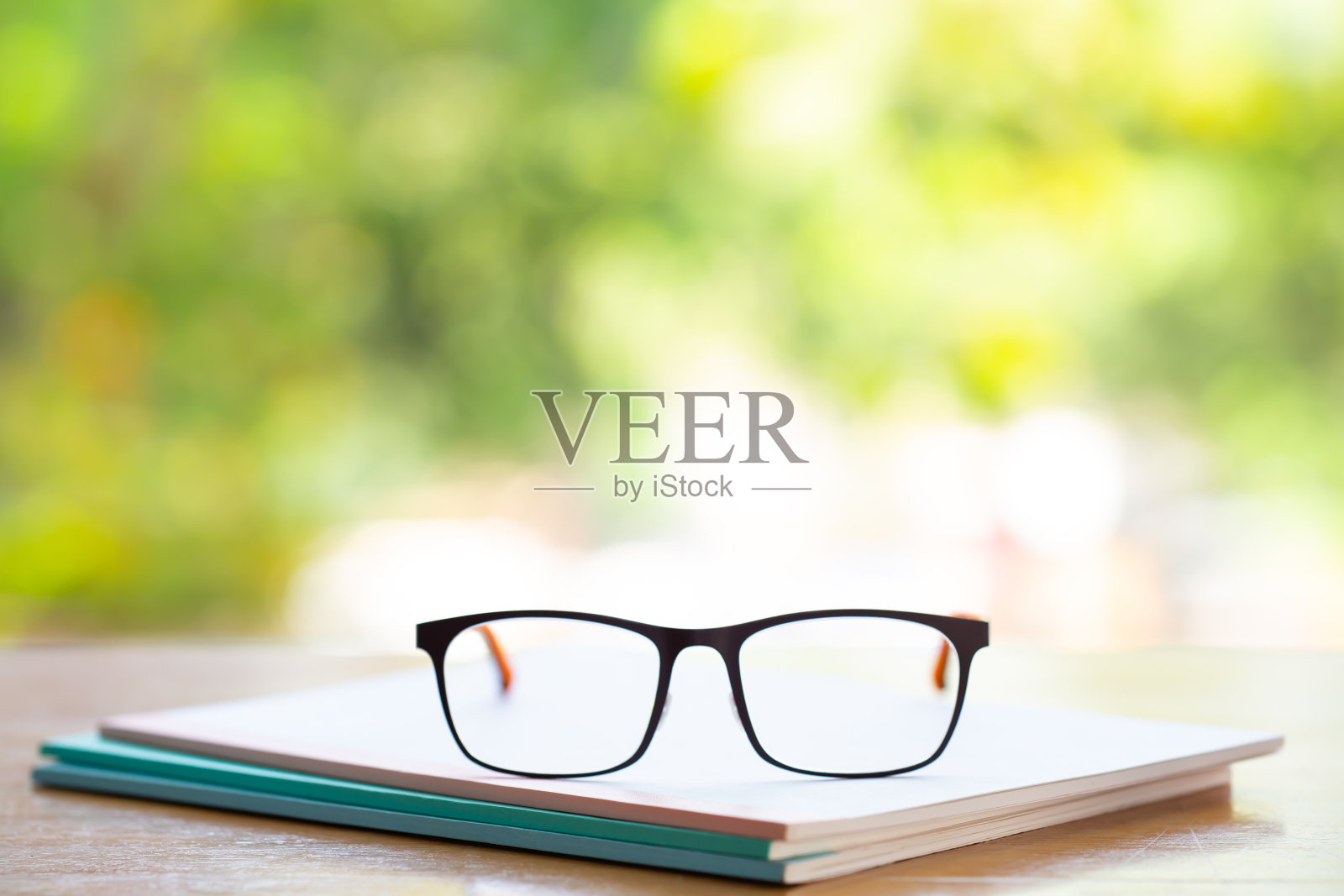 黑色眼镜和三个白色笔记本在木桌上，散景花园背景，近距离微距拍摄，选择性聚焦，文具概念照片摄影图片