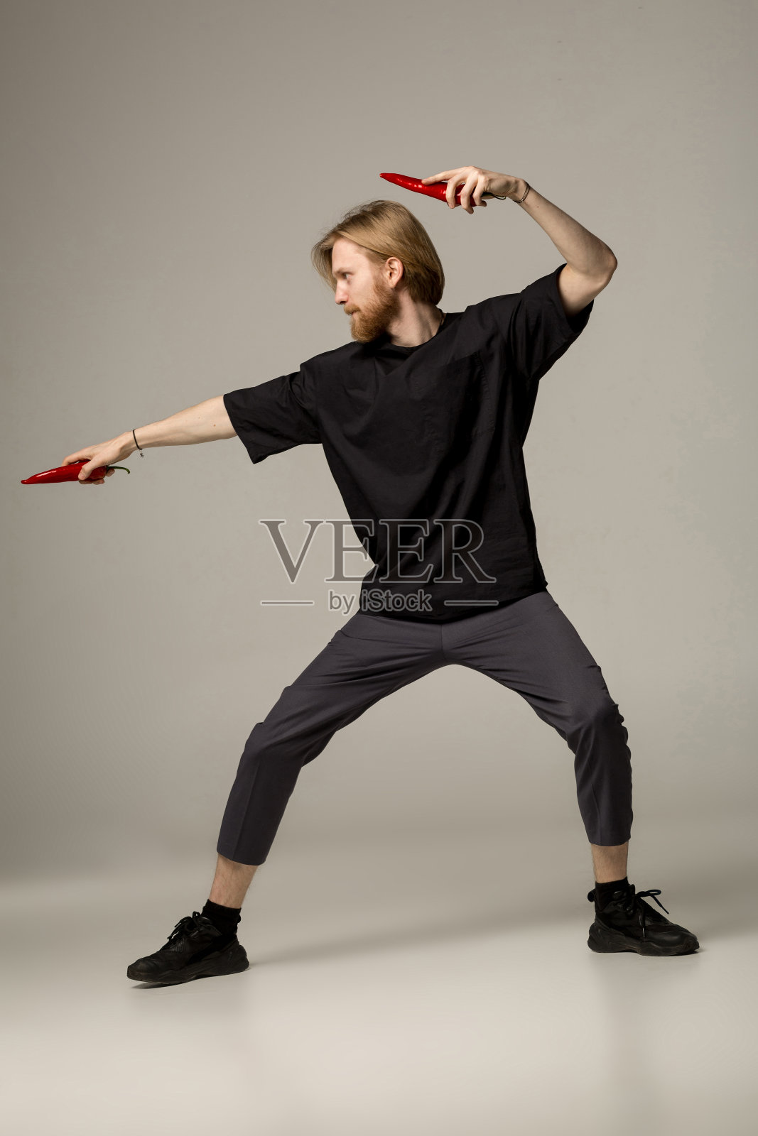 年轻的空手道大师在黑衣摆姿势与两个红辣椒在手里照片摄影图片