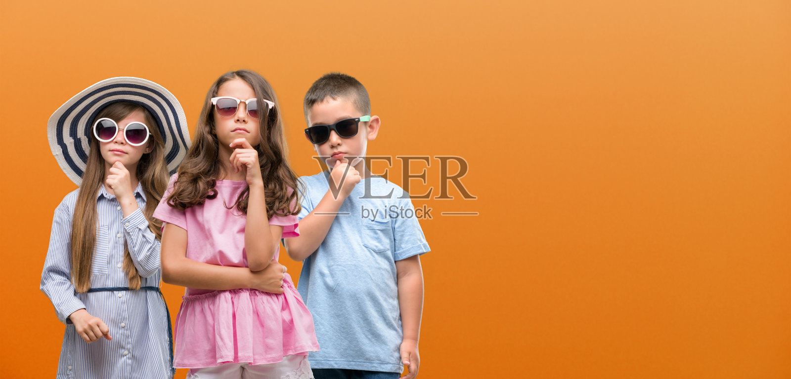 一群男孩和女孩的孩子在橙色的背景严肃地面对思考问题，非常困惑的想法照片摄影图片