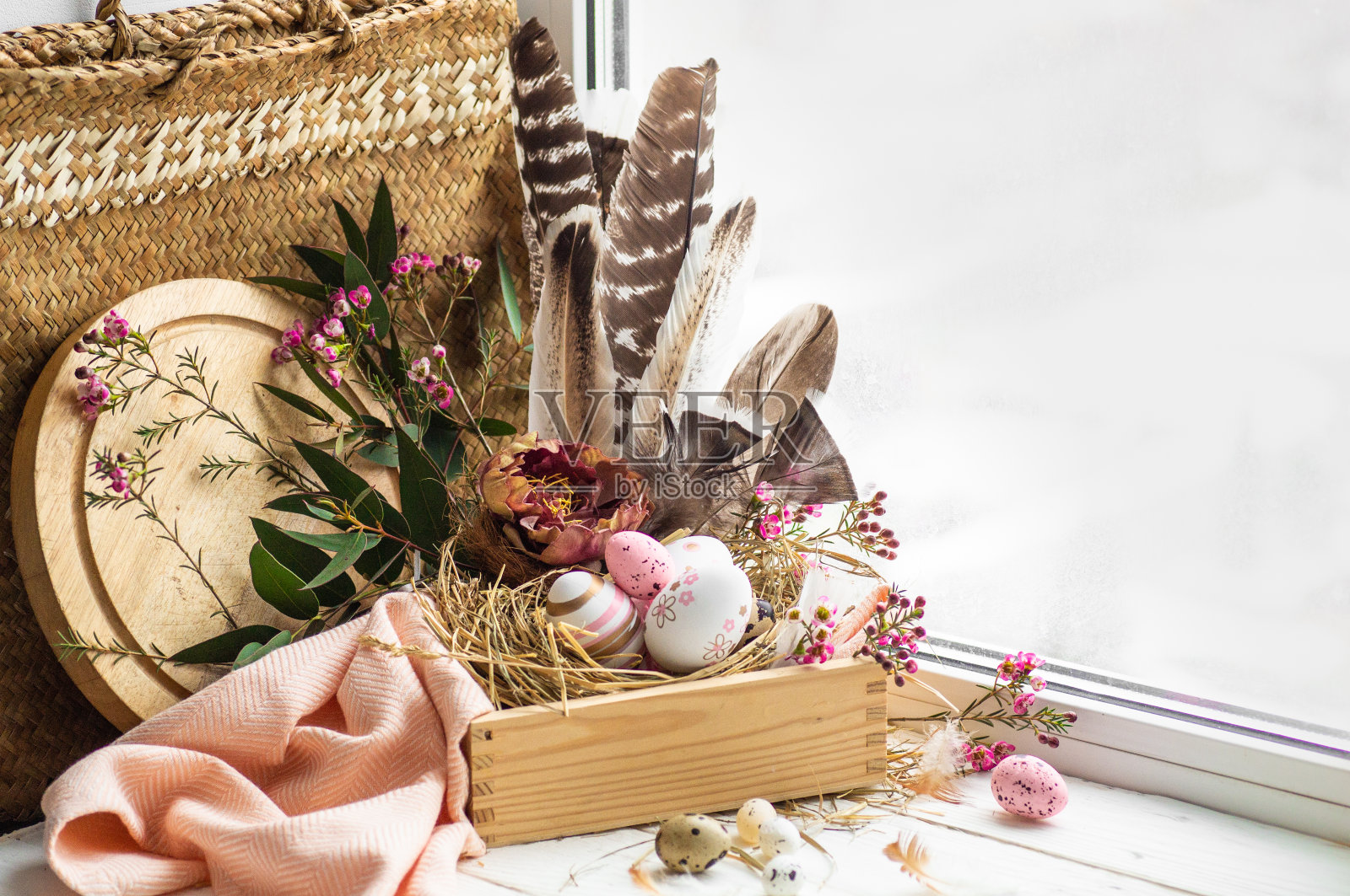 复活节快乐背景。粉红色的复活节彩蛋放在一个有花卉装饰和羽毛的巢中，靠近窗户照片摄影图片