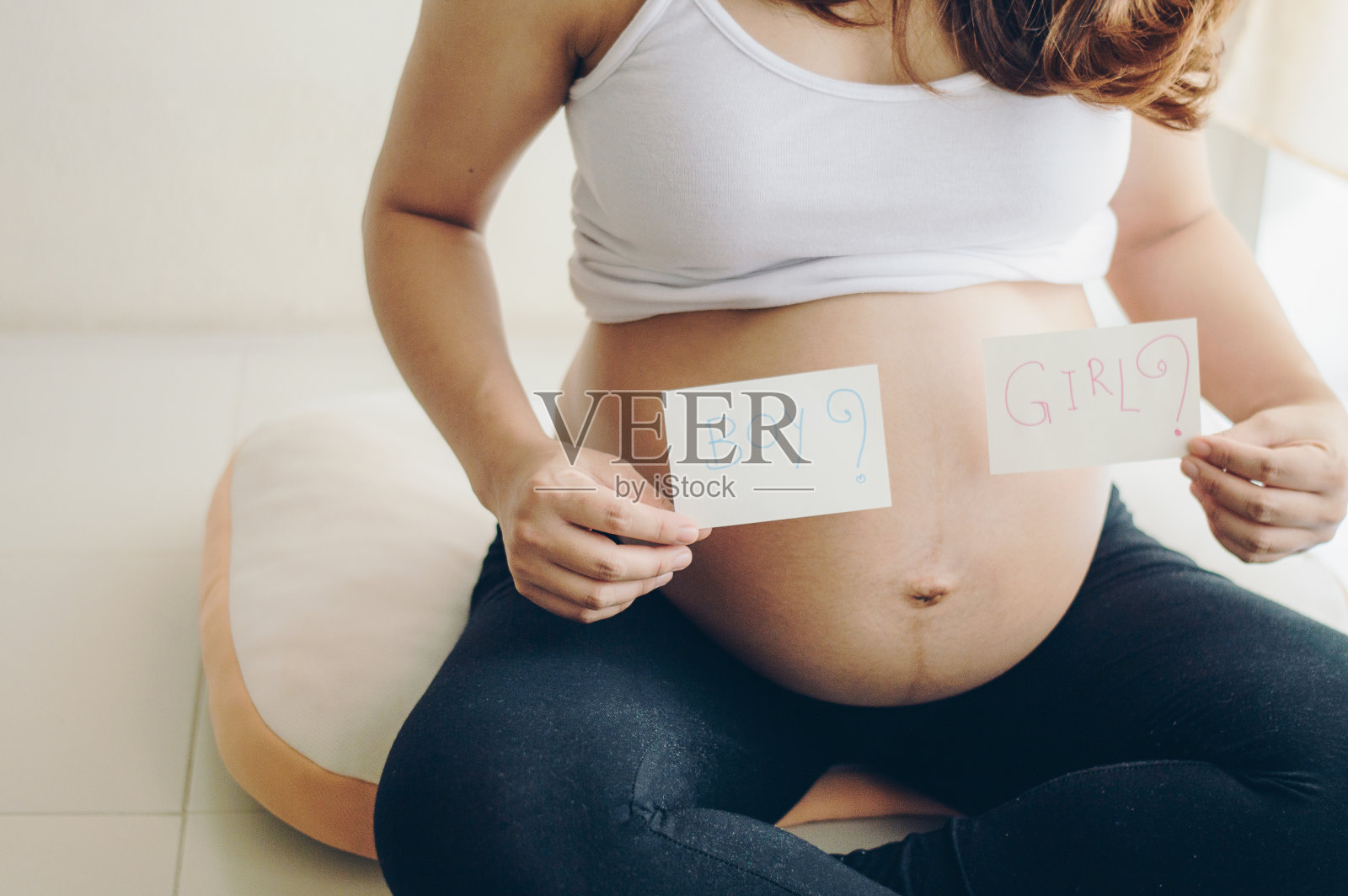 孕妇展示写有“男孩”或“女孩”字样的纸张，询问他人关于她孩子性别的裁剪照片照片摄影图片