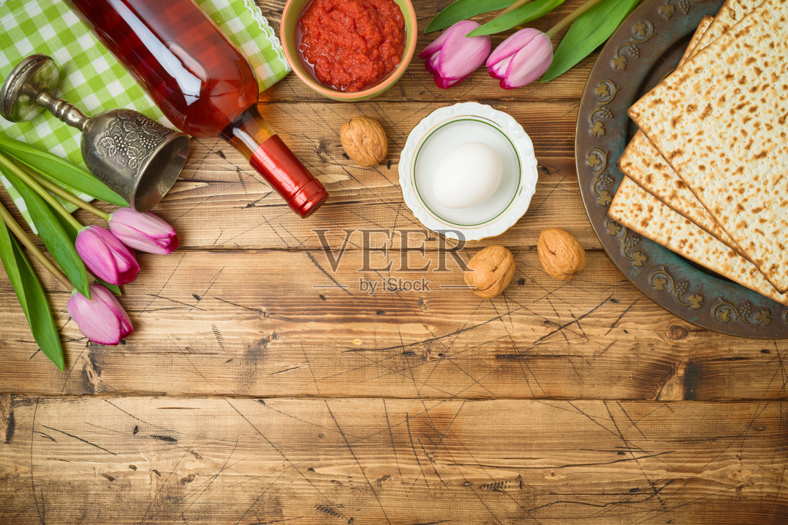 犹太节日逾越节背景与matzo，逾越节餐盘，葡萄酒和郁金香花在木桌上。照片摄影图片