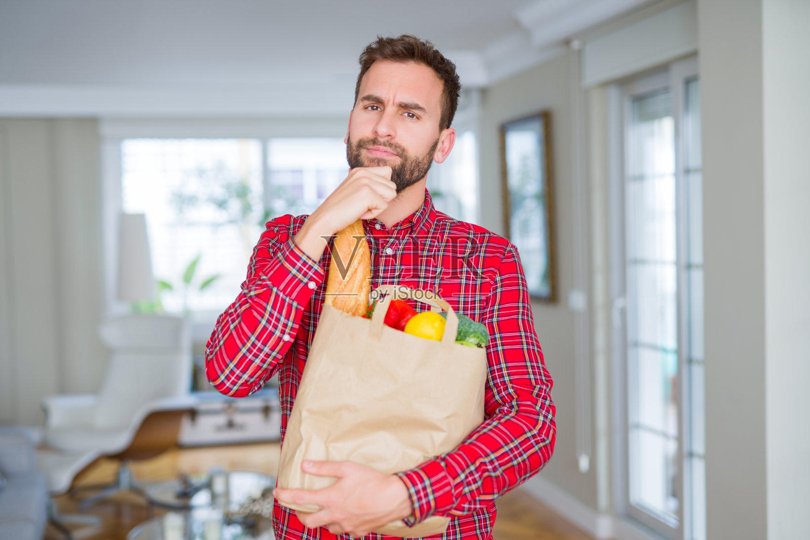英俊的男子拿着杂货袋严肃的面对思考问题，非常困惑的想法照片摄影图片