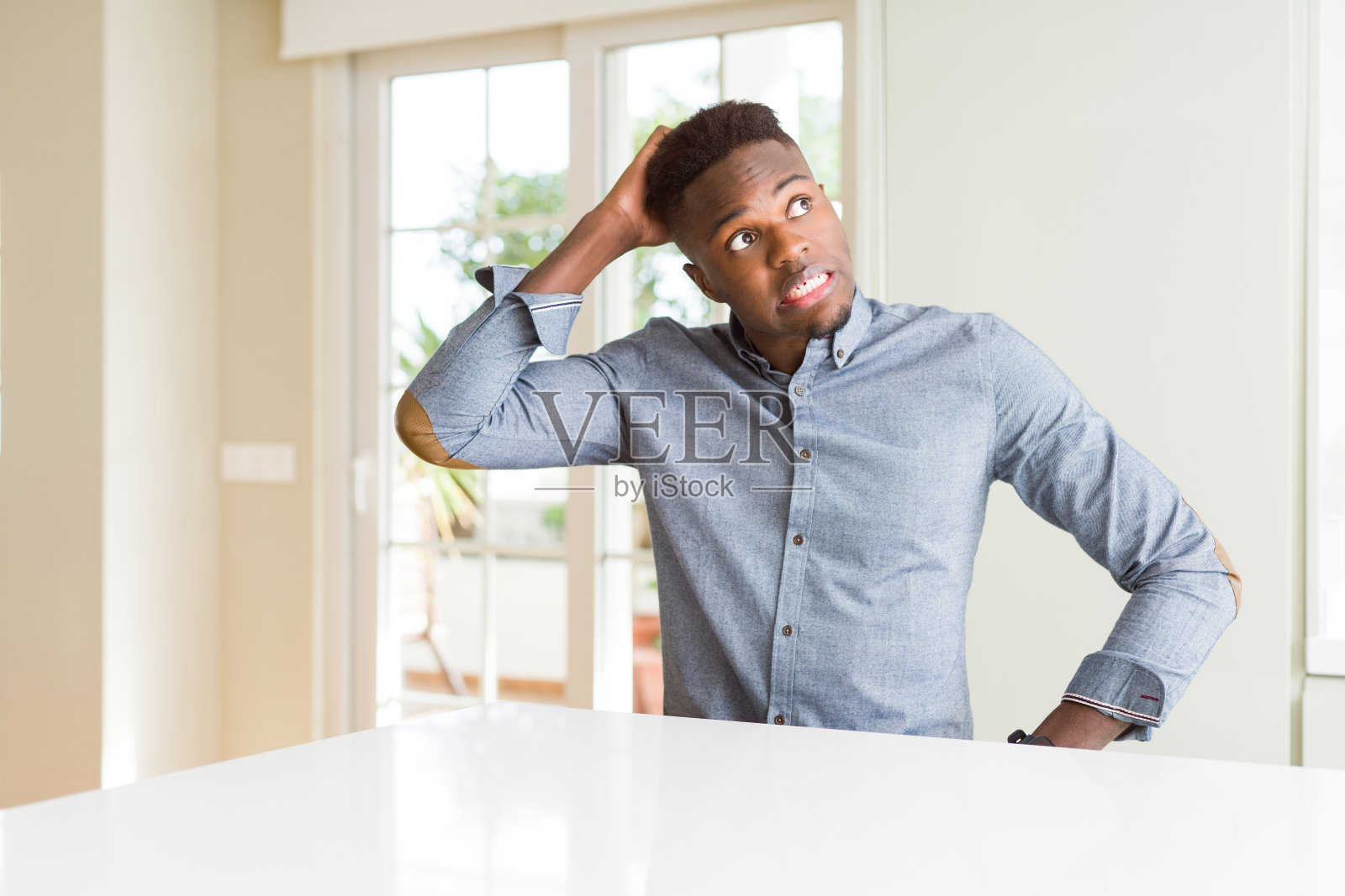 英俊的非裔美国人在白色的桌子上困惑和好奇的问题。不确定用怀疑，用手思考。沉思的概念。照片摄影图片