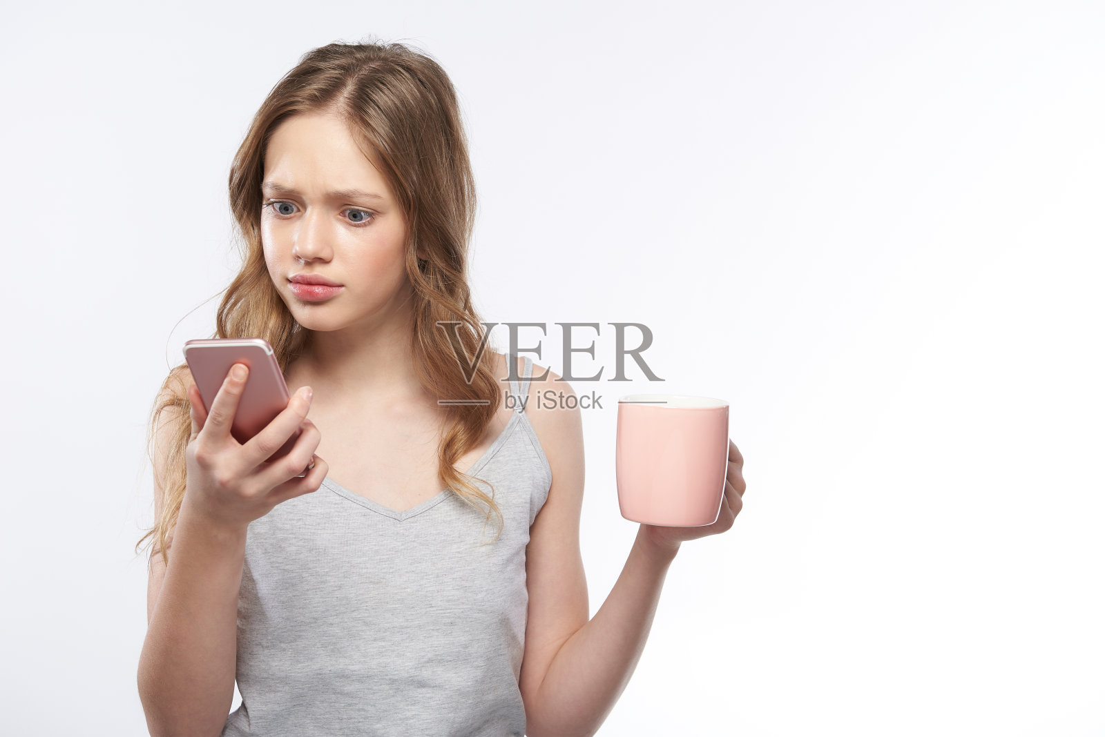 震惊的少女拿着一杯咖啡，同时使用手机照片摄影图片