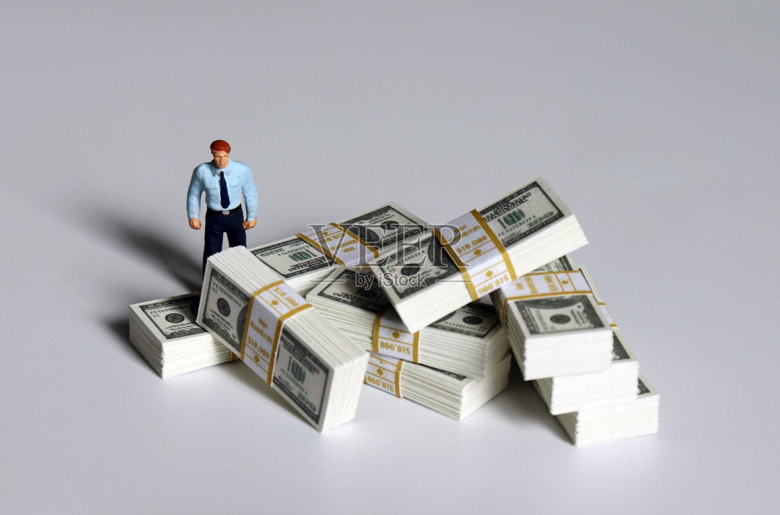 一堆百元大钞和一个站着的小人。照片摄影图片