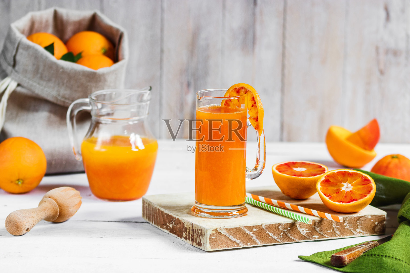 木桌上放着一杯新鲜榨橙汁和血橙。阳光明媚的夏日心情。照片摄影图片