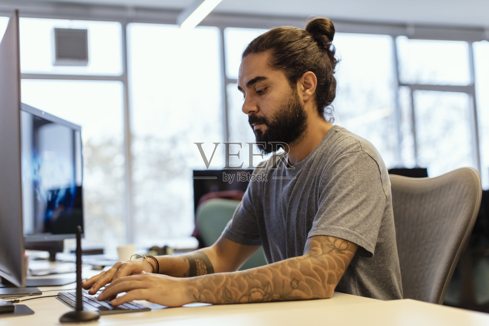 手有纹身的时尚潮人的肖像，在办公室的电脑上写笔记照片摄影图片