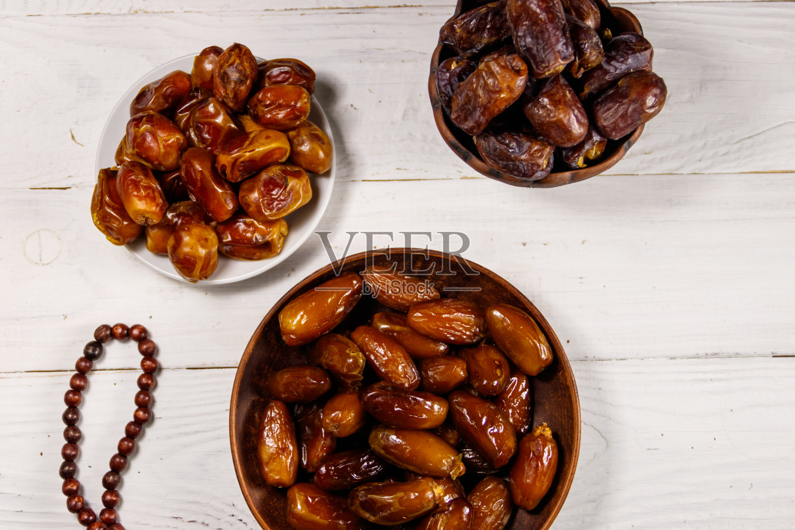 白色木桌上放着红枣、水果和念珠。俯视图照片摄影图片