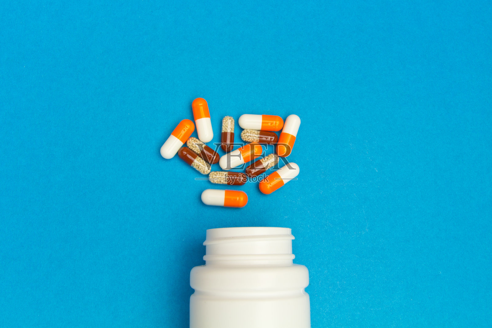 胶囊(药丸)从蓝色背景的白色瓶子里倒出来。医学背景,模板。照片摄影图片