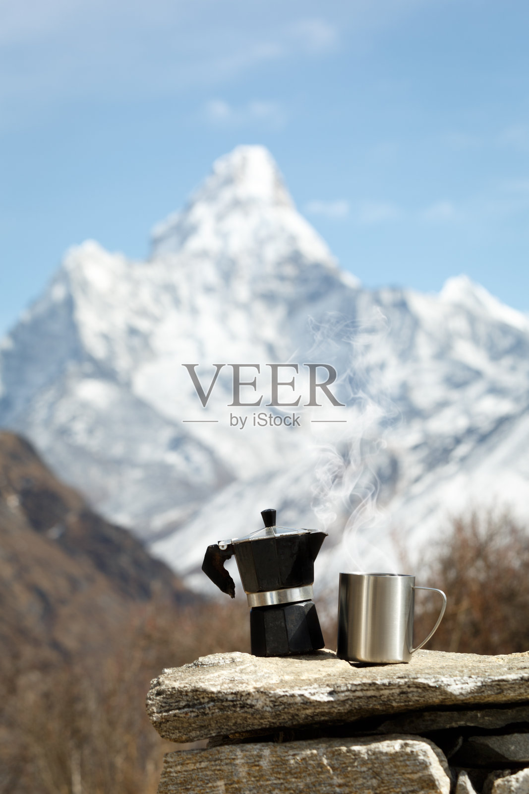 马克杯和咖啡壶放在石头上。山被弄模糊了。蒸汽从杯子里冒出来。Ama Dablam。珠峰登山照片摄影图片