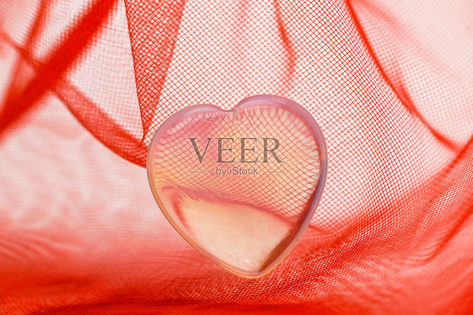 情人节。红色透明织物上镶嵌着一颗小小的透明塑料心照片摄影图片