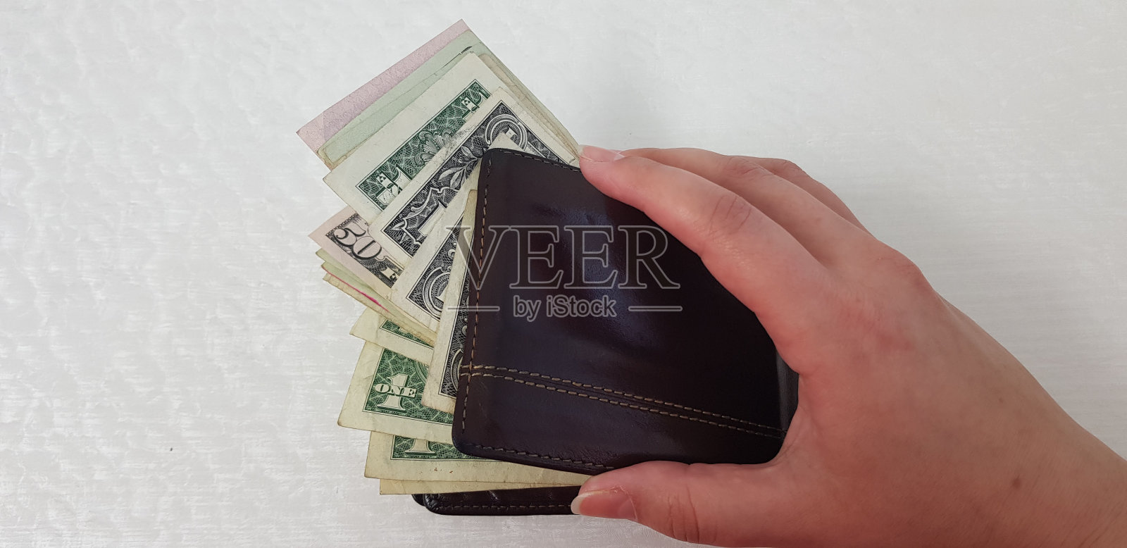 白色背景下，女人手打开装满美元的棕色皮夹照片摄影图片