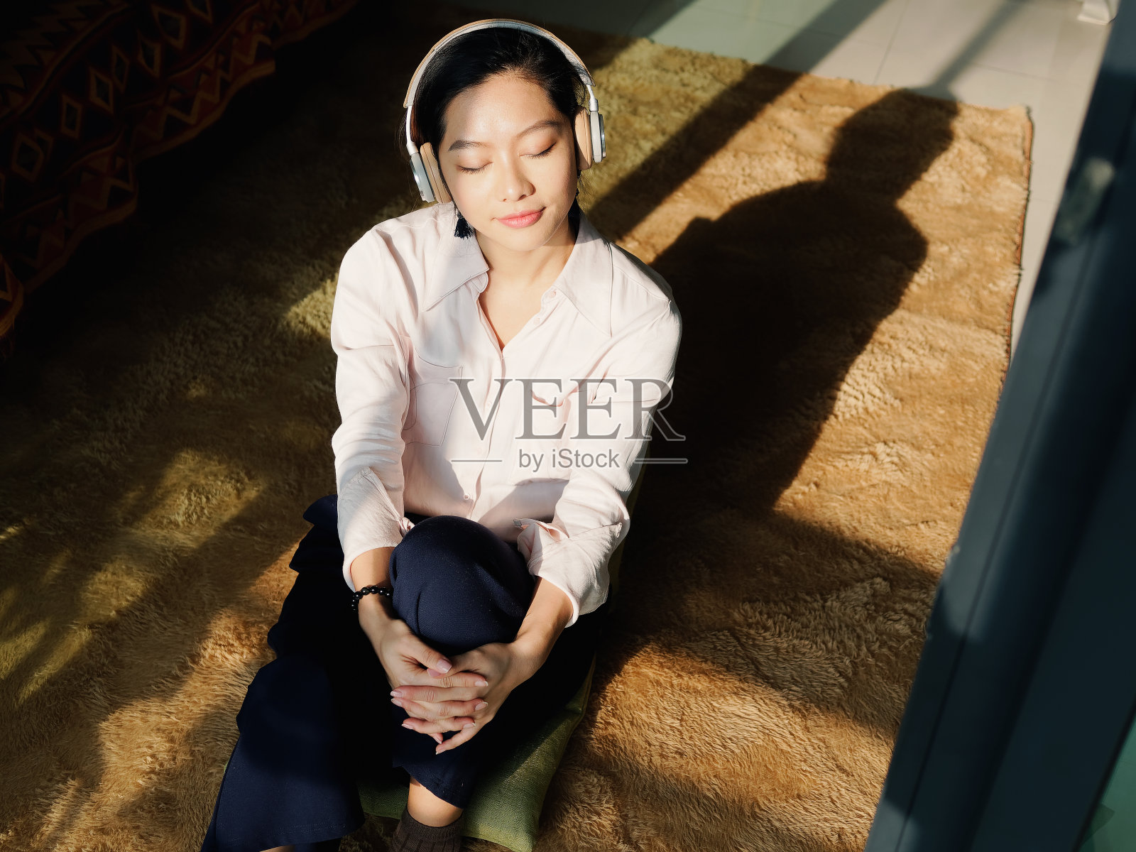 阳光明媚的日子里，穿着白衬衫的漂亮年轻女子坐在家里欣赏音乐。肖像魅力中国开朗时尚女孩，情感，人，美丽和生活理念。照片摄影图片