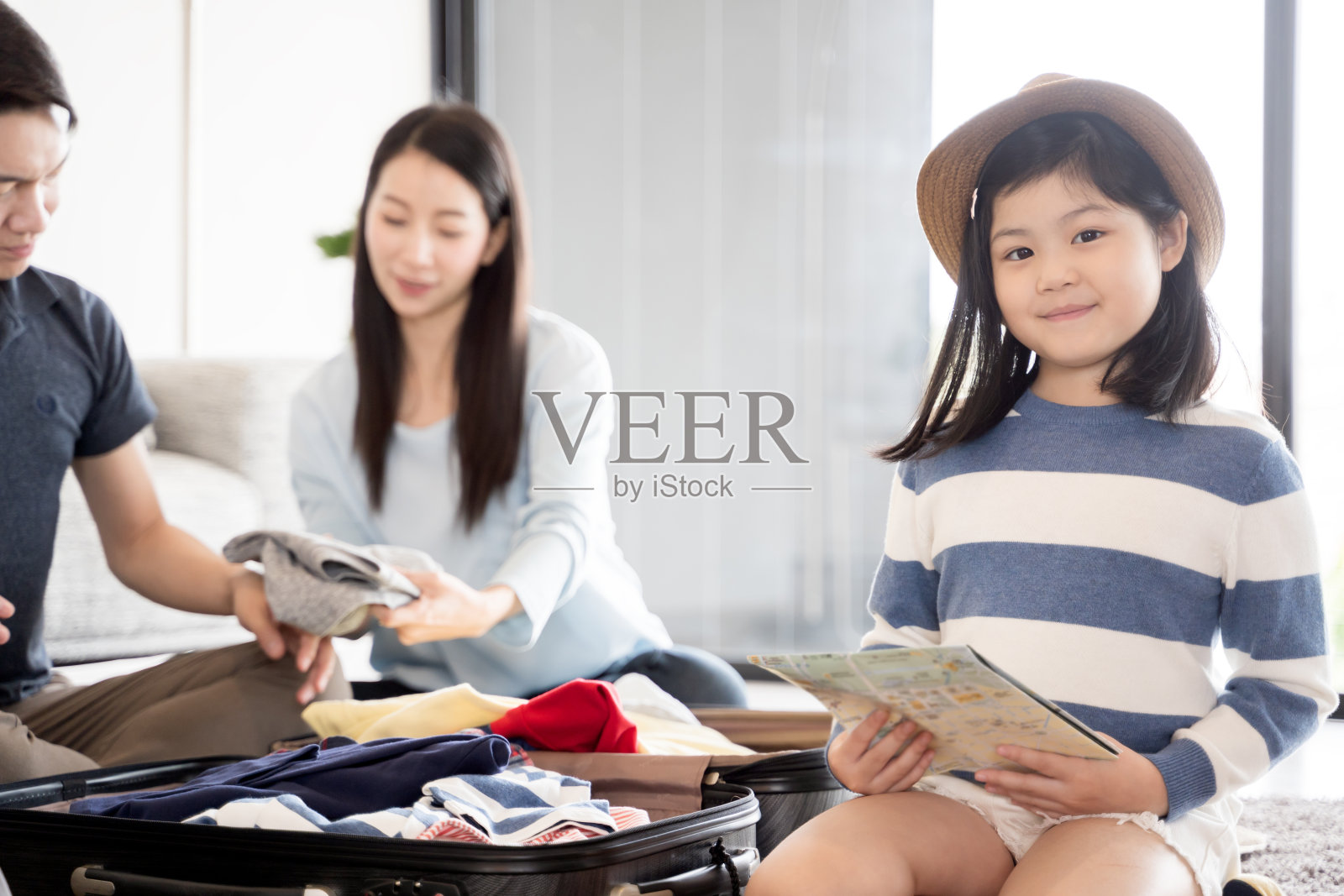 快乐的亚洲家庭在家里准备旅行。妈妈，女儿和爸爸正在为旅行打包行李照片摄影图片