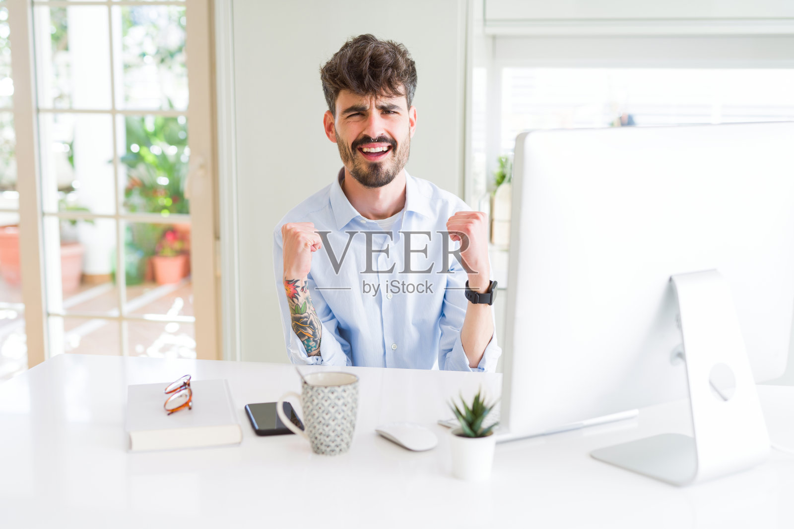 年轻的商人使用电脑工作，非常高兴和兴奋做胜利者的姿态，手臂举起，微笑和尖叫的成功。庆祝活动的概念。照片摄影图片