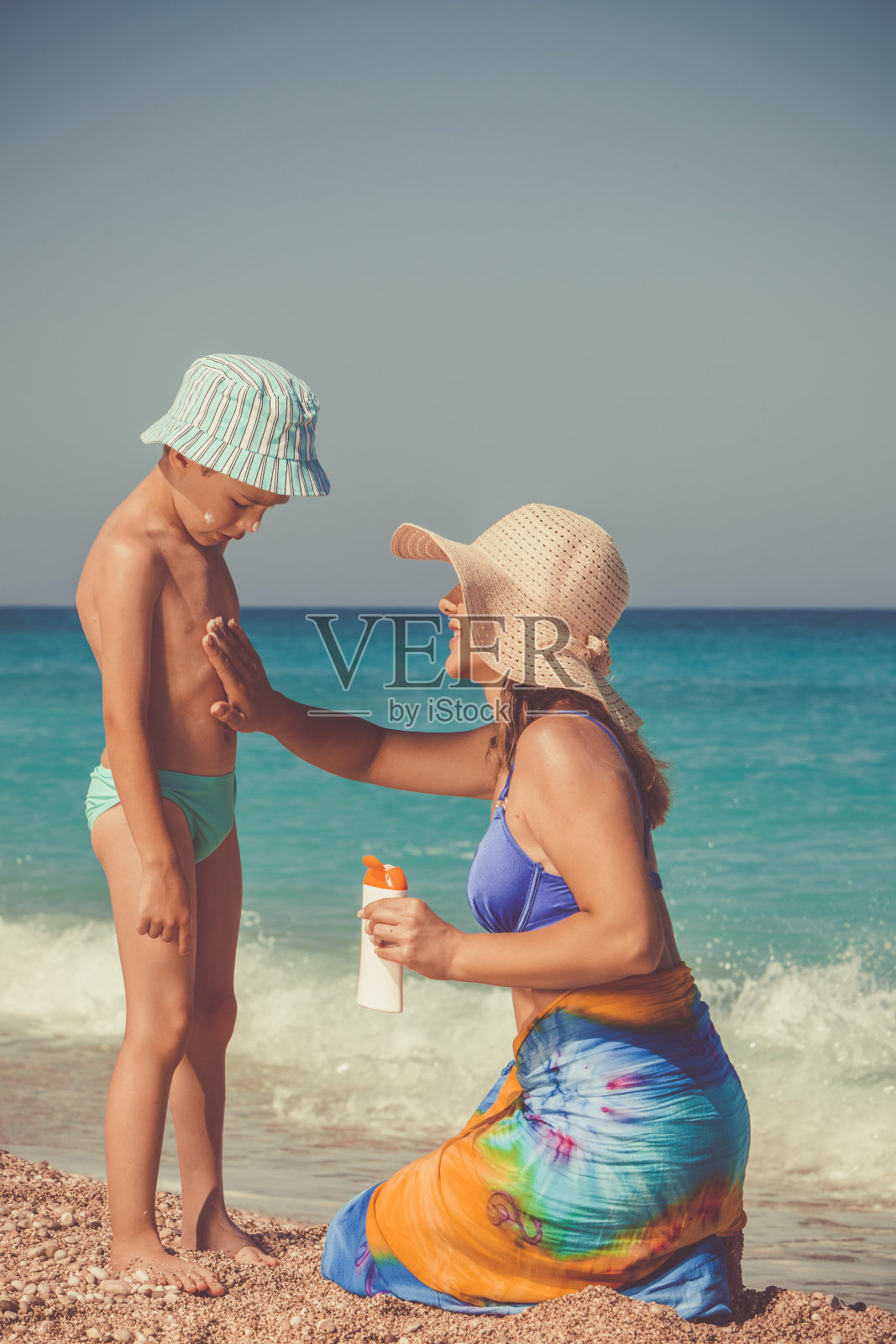 在海滩上，母亲正在给她的孩子涂防晒霜照片摄影图片