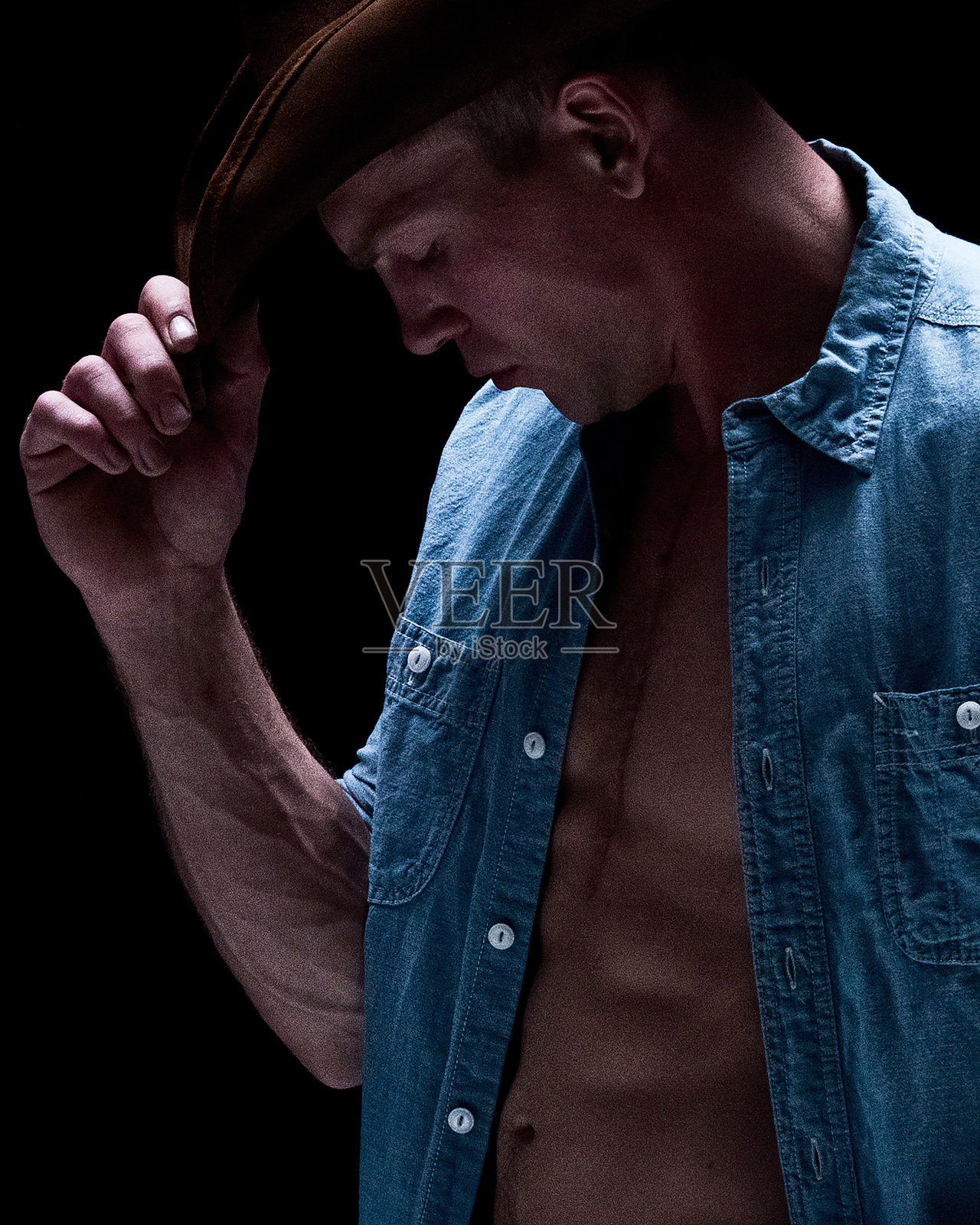 有男子气概的牛仔，衬衫敞开，戴着帽子照片摄影图片