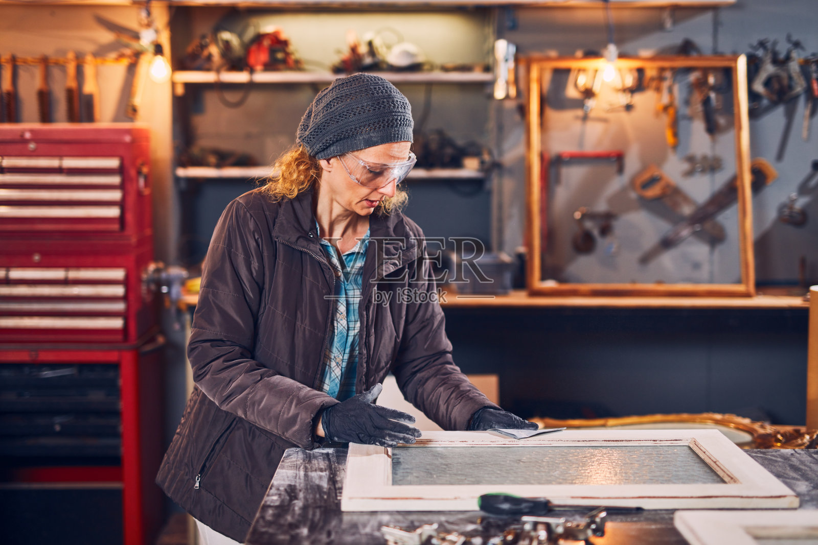 在一个复古的车间里，一个女木匠在打磨旧窗户。照片摄影图片