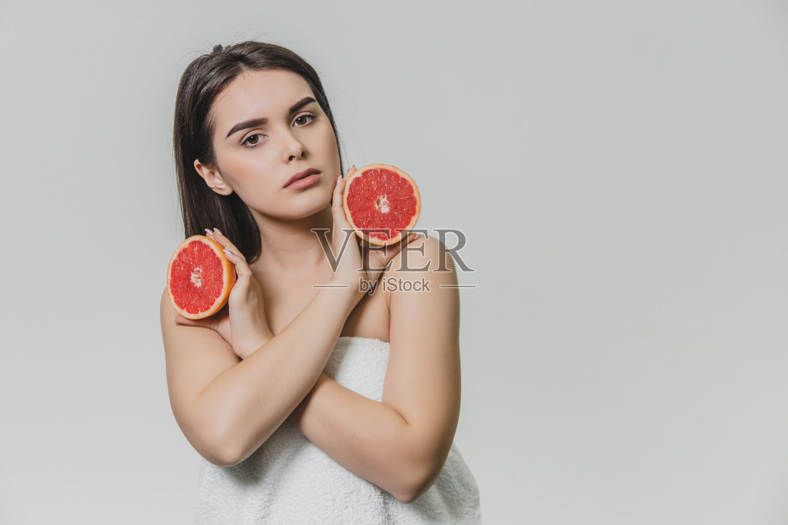 一个快乐的女孩用两半葡萄柚围在脸上。她微笑着，期待着幸福。孤立在背景中照片摄影图片