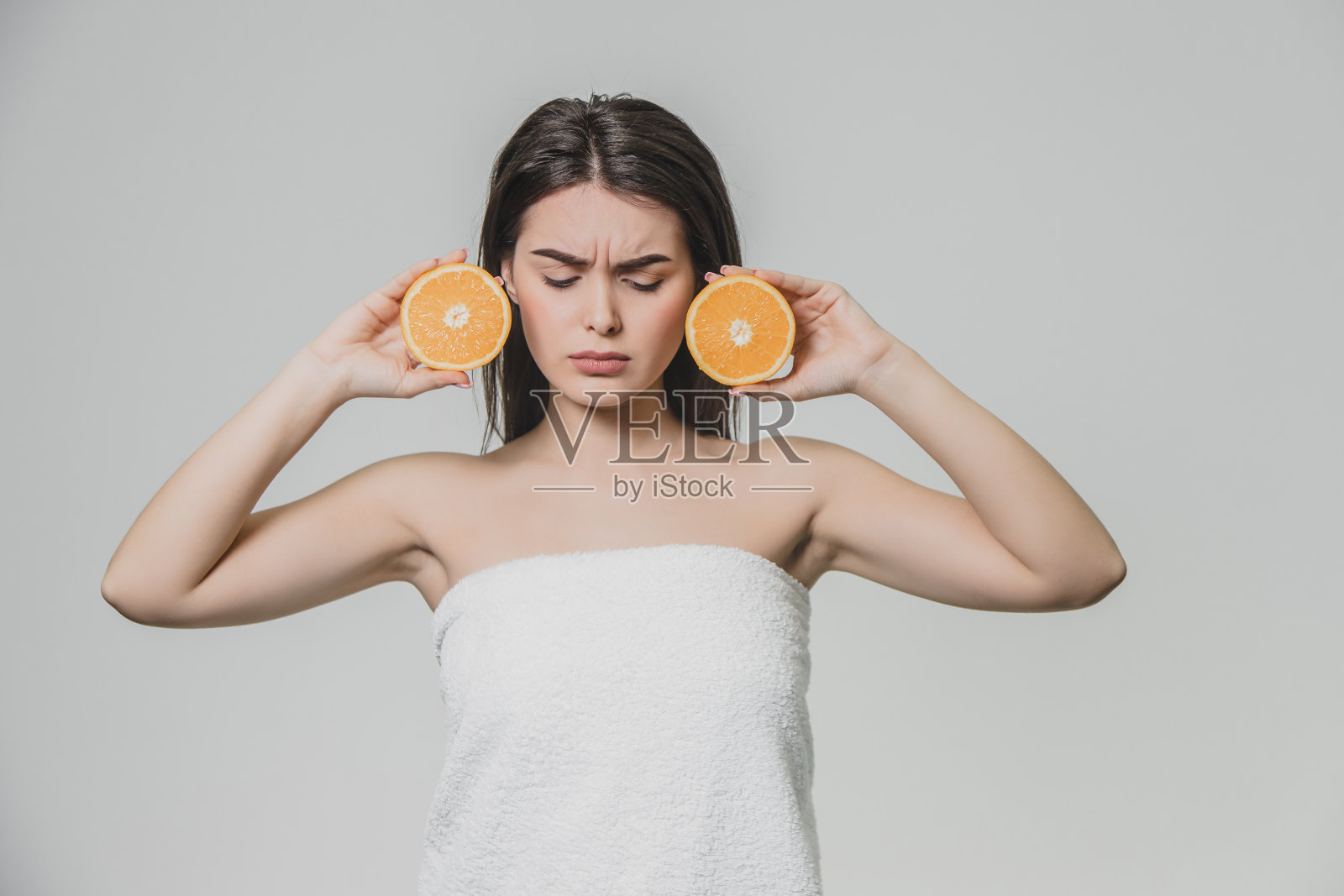 快乐的年轻女孩与水果摆姿势。在这期间，她向下看。手里拿着两块橘子，很严肃。照片摄影图片