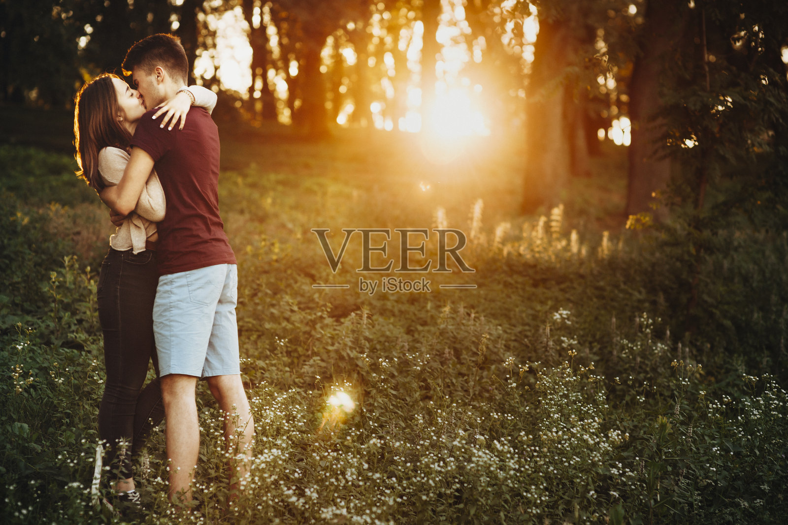 一个可爱的年轻欧洲夫妇的全长肖像，拥抱和亲吻在森林外面的日落，而约会。照片摄影图片