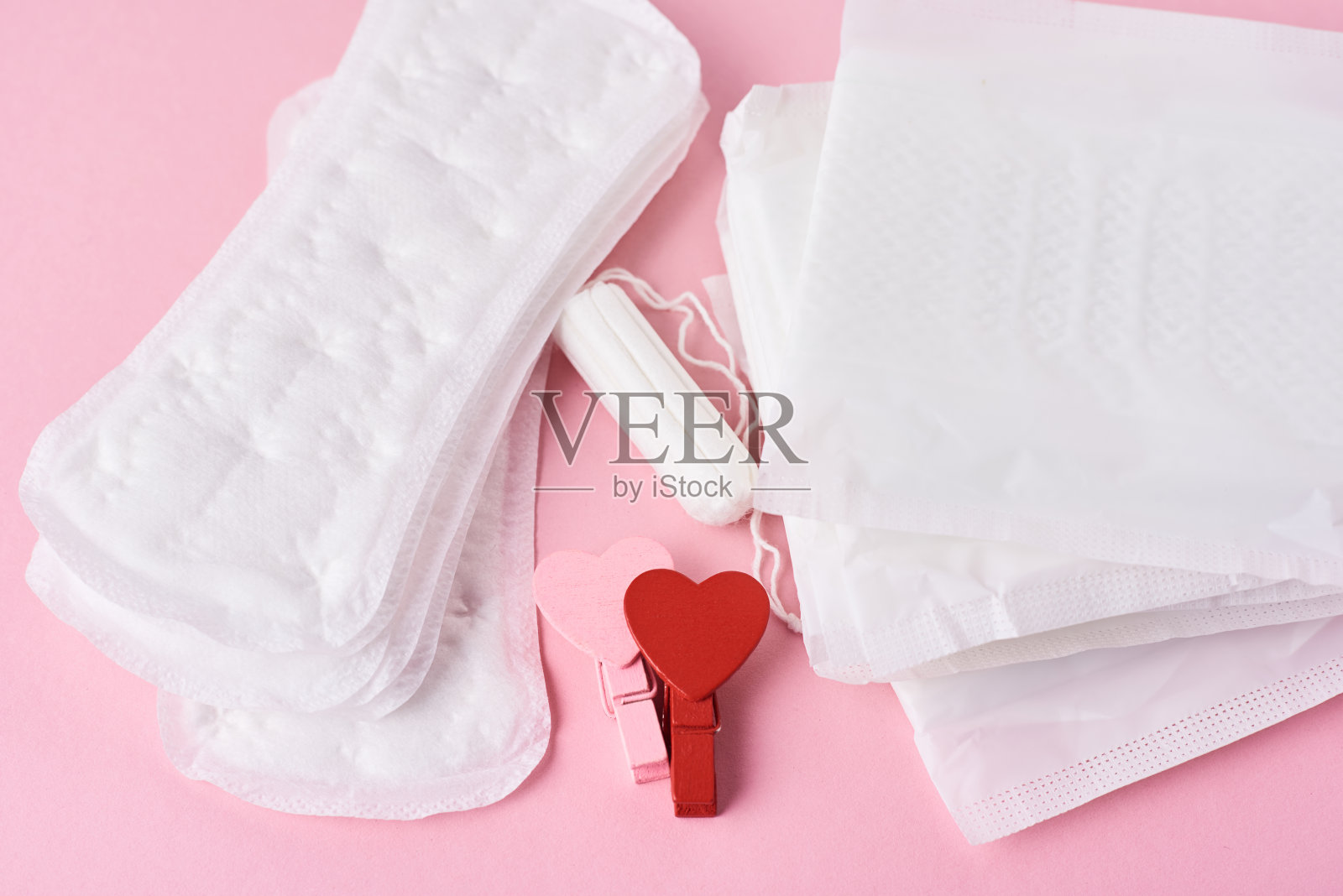 卫生巾，月经卫生棉条和粉色背景上的木质红心，俯视图照片摄影图片