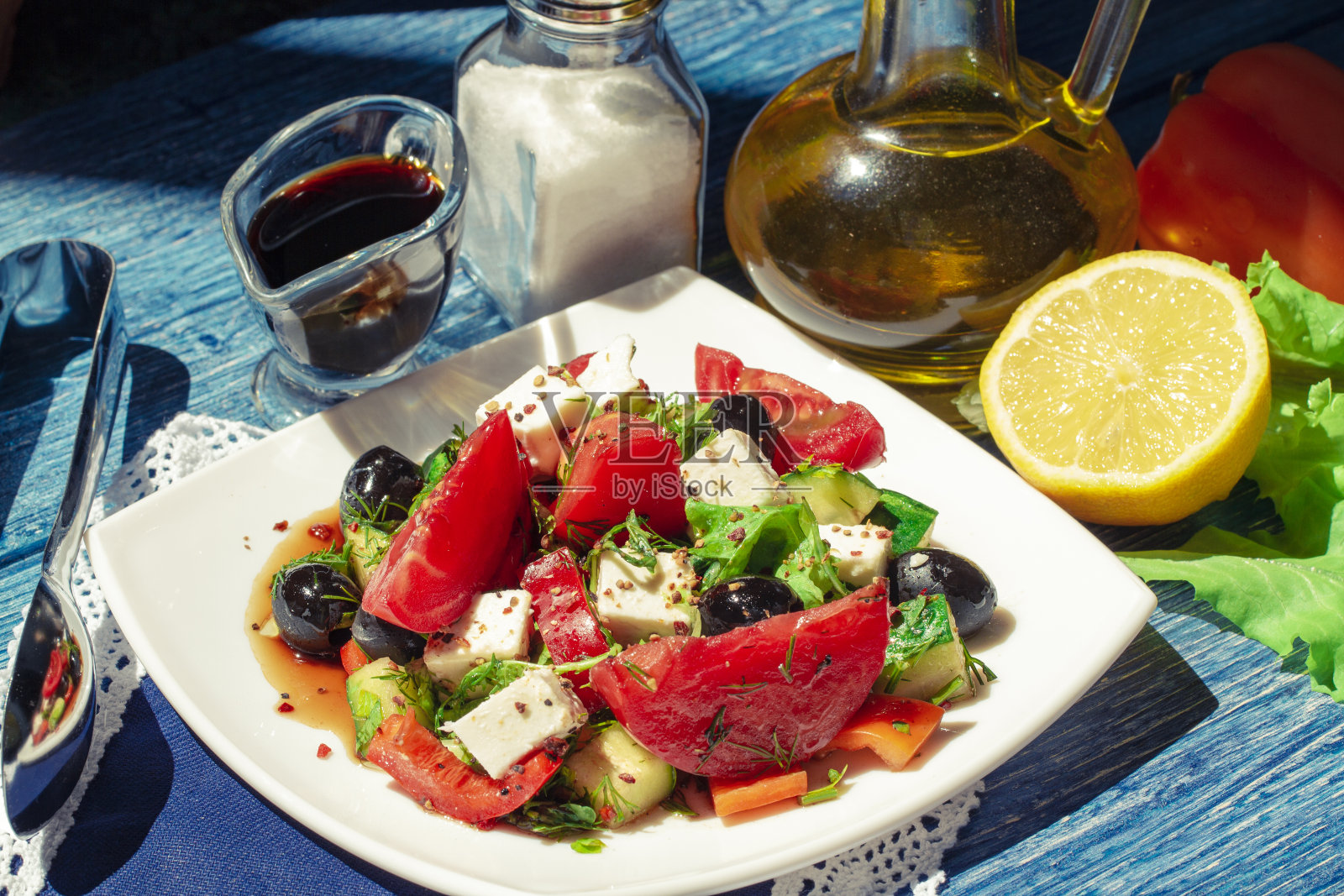蔬菜沙拉在碗里，在蓝色的木桌上。美味的希腊沙拉，羊乳酪，橄榄和西红柿在碗里。明亮的日光。传统的希腊沙拉配新鲜蔬菜，羊乳酪和橄榄。照片摄影图片