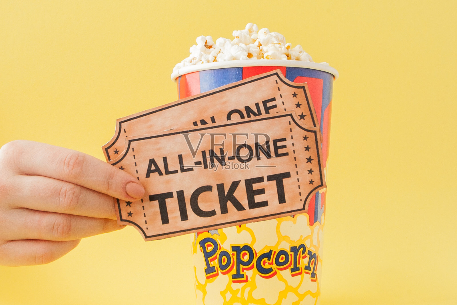 Hand从一个黄色背景的纸杯里拿出一张电影票和爆米花。女人吃爆米花。电影的概念。平的。本空间照片摄影图片