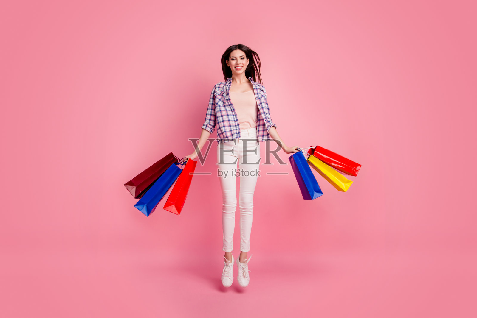 全身的身体尺寸照片美丽的她她女士跳高的手手臂购买惊人的商场黑色星期五穿鞋帽子休闲格子衬衫白色牛仔裤牛仔孤立的粉色背景照片摄影图片