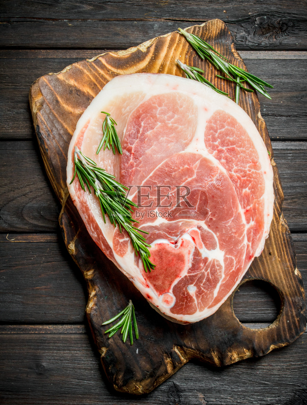 大块生猪肉和迷迭香放在切菜板上。照片摄影图片