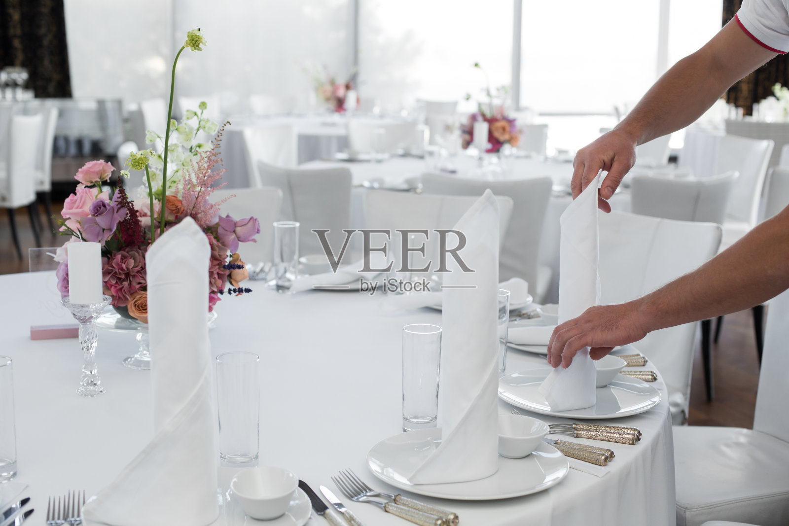 餐厅里的服务员为客人摆了一张桌子。侍者的手中是一块白色的桌布，餐巾，白色的盘子和一束花放在桌子的相框里照片摄影图片