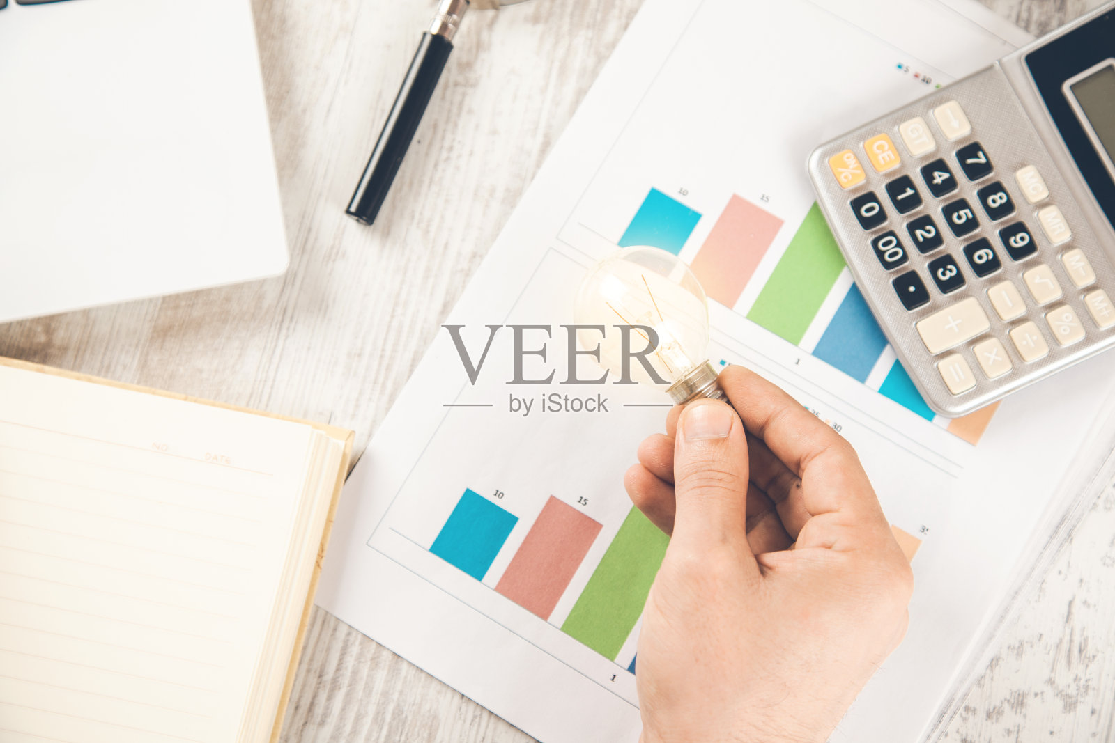 男人的手灯泡在图表上的办公桌上照片摄影图片